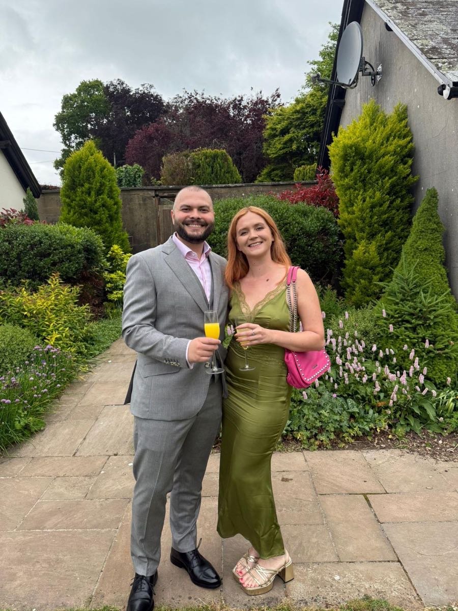 Rachael and Peter smiling together in a garden, raising glasses of fizz